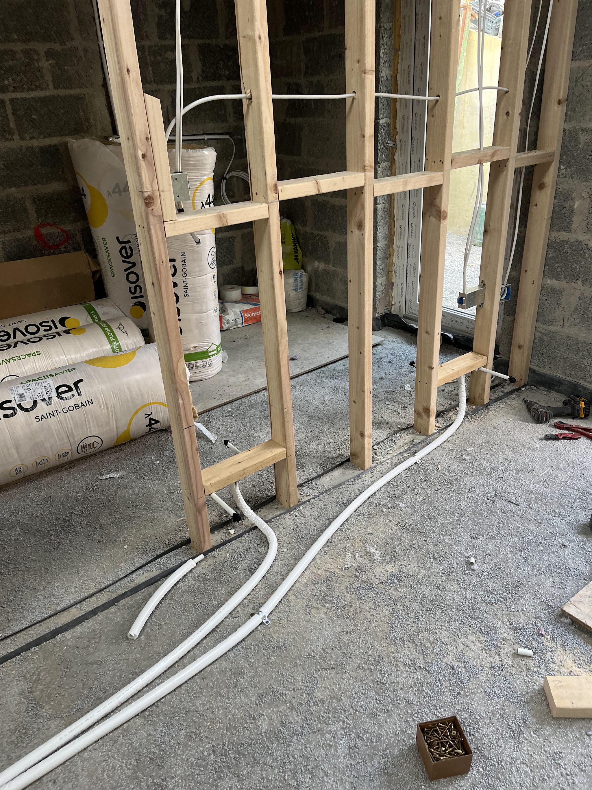 First-fix pipework laid on a concrete floor beside a timber stud wall