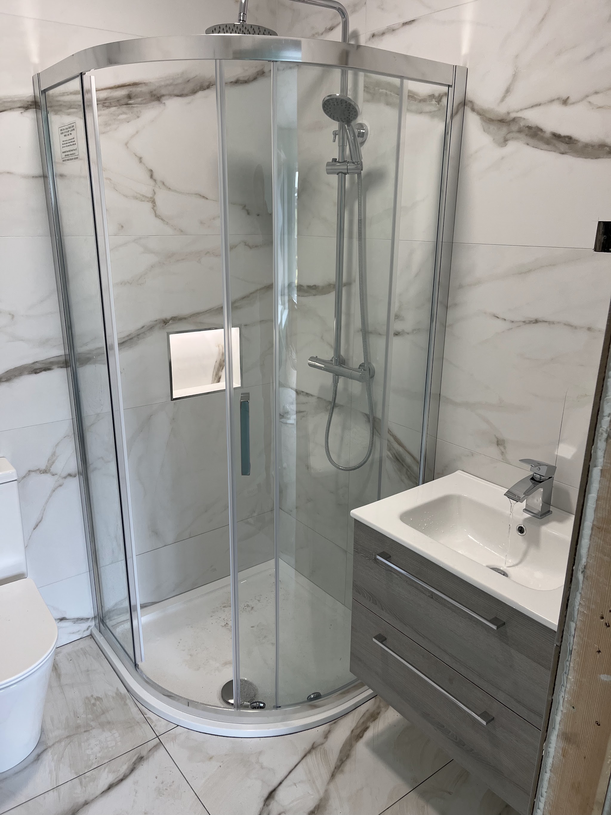 Corner shower enclosure with a rain shower and a wall-hung basin on marble-effect tiles