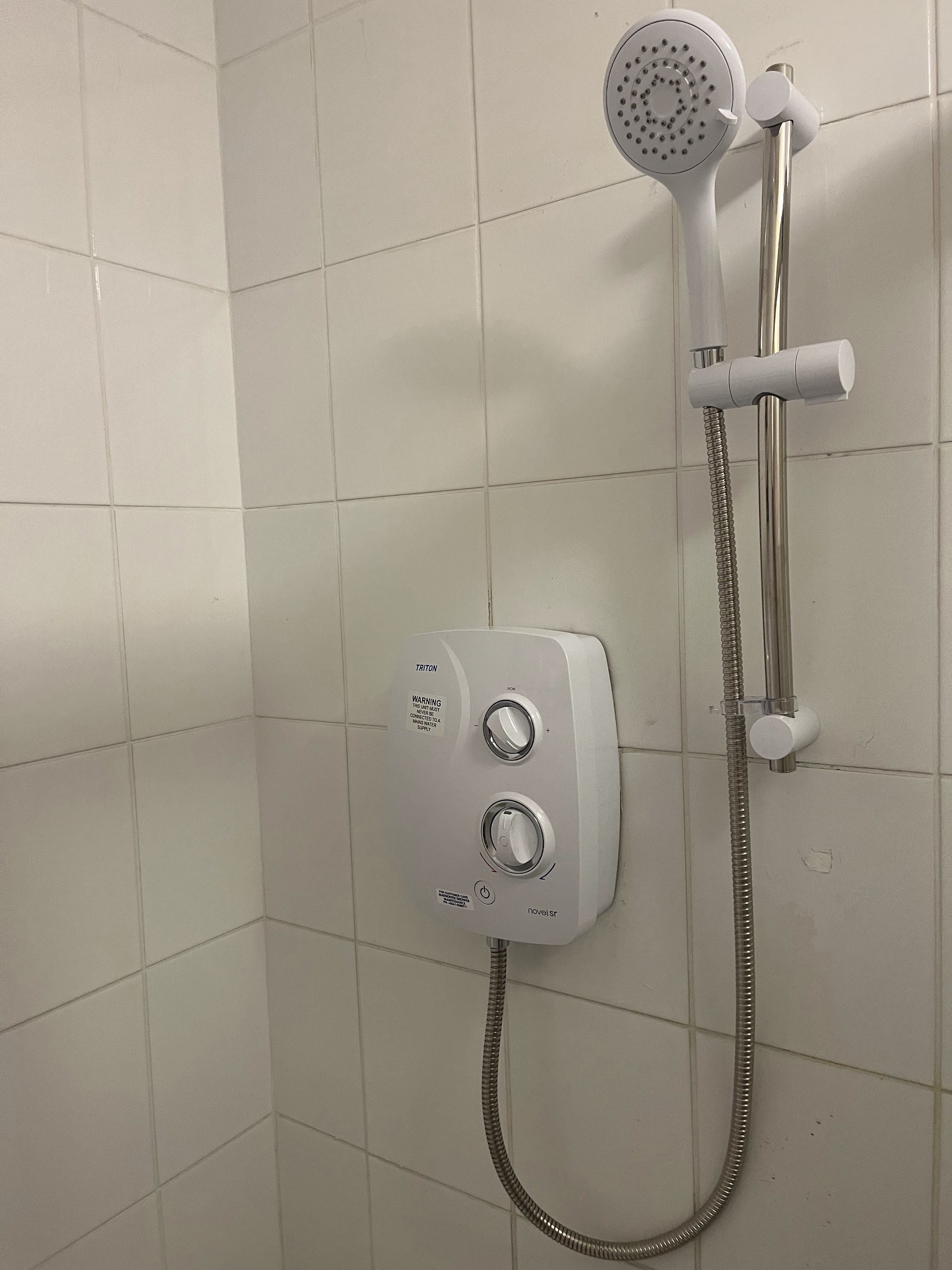Electric shower with a slide rail and handset fitted on white wall tiles